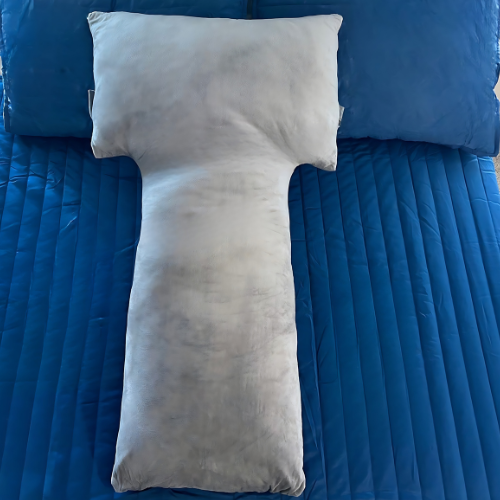 This image showcases the Special T Pillow laid out on a blue bedspread, emphasizing its distinctive T-shape. The pillow's grey velvet cover and ergonomic design are highlighted, illustrating its appeal for providing targeted support and enhancing sleep comfort.